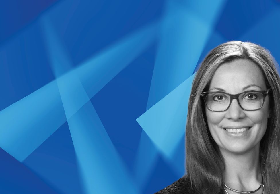 Professional headshot of smiling woman with glasses against blue geometric background